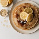 A mouth-watering stack of pancakes topped with lemon slices and surrounded by almond flakes.